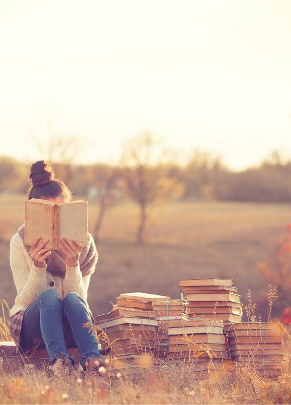 woman in field with piles of books reading